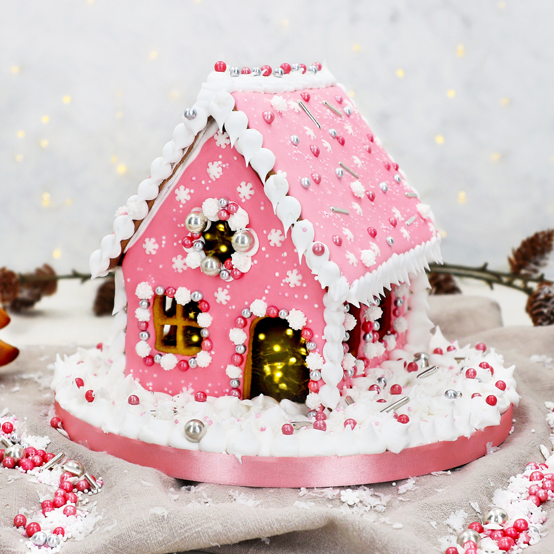 Das Bild zeigt ein pinkes Lebkuchenhaus mit zuuckersüßen Dekorationen.