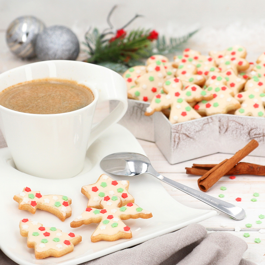 Das Bild zeigt süße Weihnachtskekse mit Glasur und bunten Streuseln.