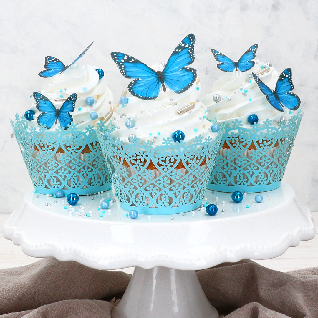 Das Bild zeigt Cupcakes auf denen blaue Schmetterlinge aus Wafer paper liegen
