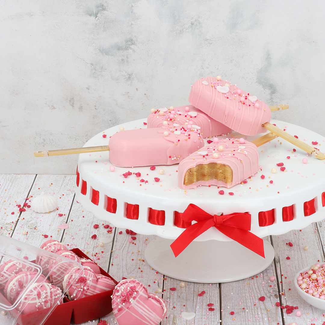 Das Bild zeigt rosa farbende Cakesicles und Macarons