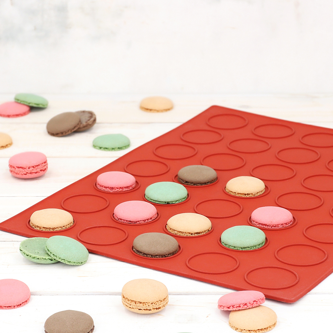 Das Bild zeigt eine Backmatte für Macarons, es sind auch einzelne Halbschalen auf der Matte verteilt.