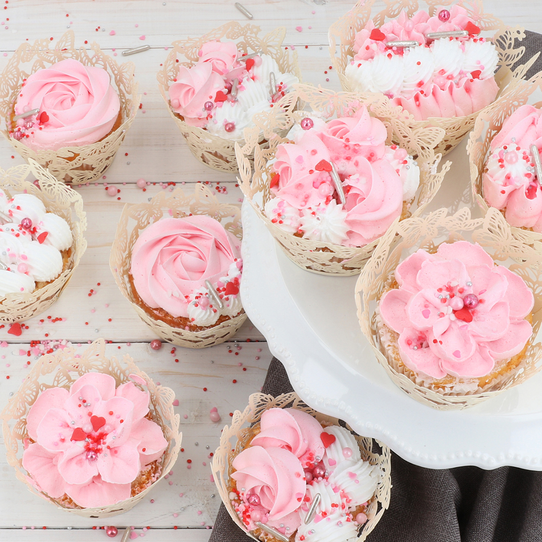 Das Bild zeigt Cupcakes auf denen mit einer weißen und rosanen Creme Blumen aufgespritzt wurden