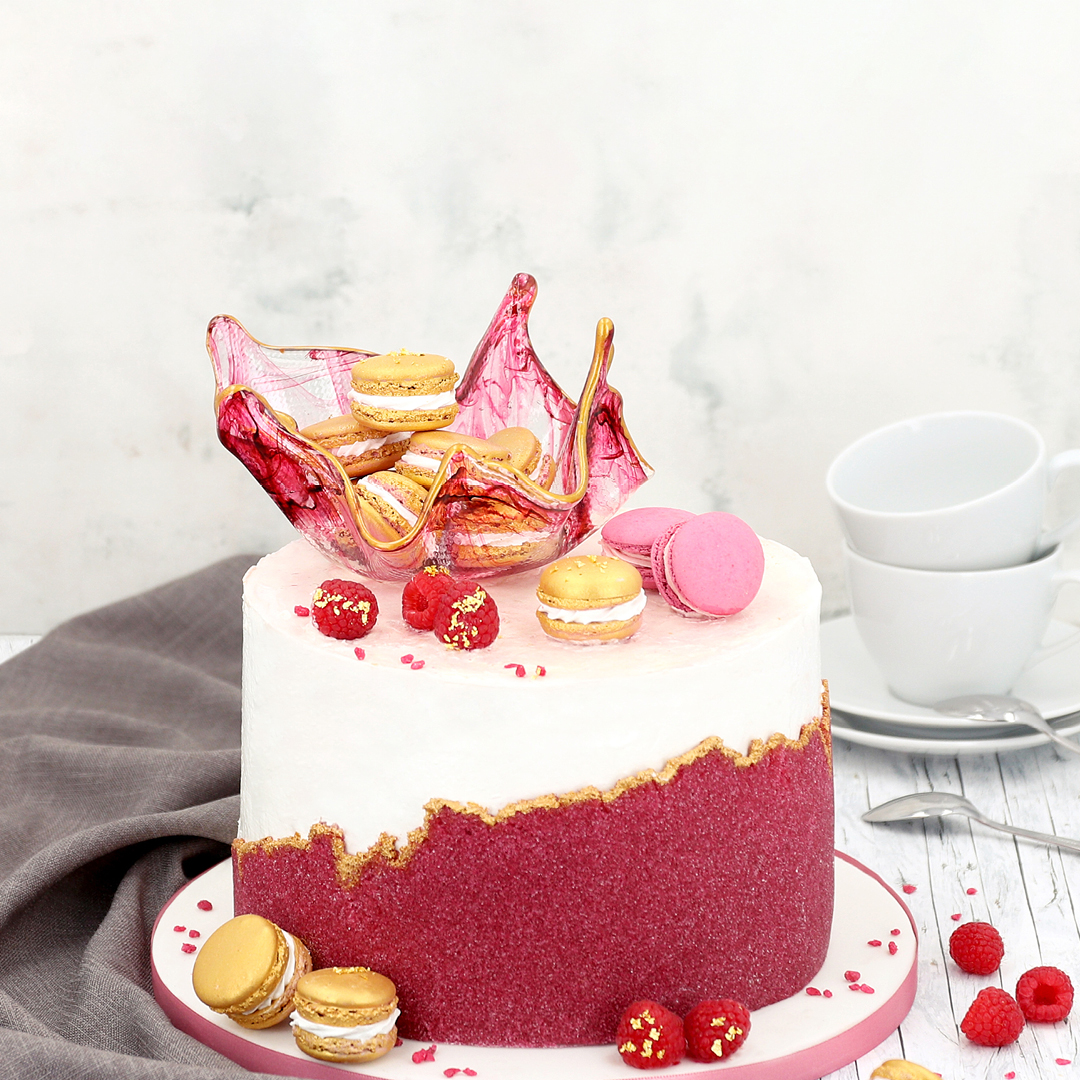 Das Bild zeigt eine Torte die mit gefärbten Zucker ummantelt wurde und einen Cake Topper aus Isomalt hat